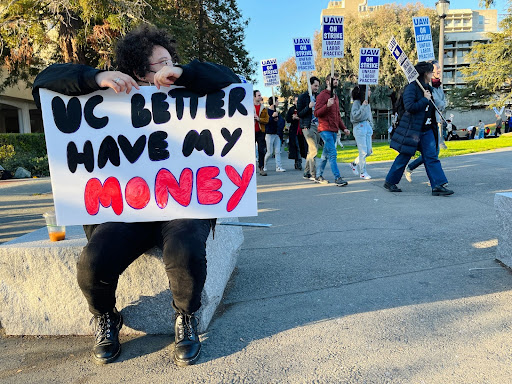 UC worker holding sign saying "UC better have my money" while sitting